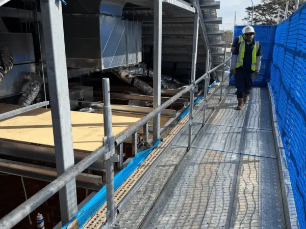 Scaffolder crossing an edge-protection platform with safety mesh on a Cowaramup site