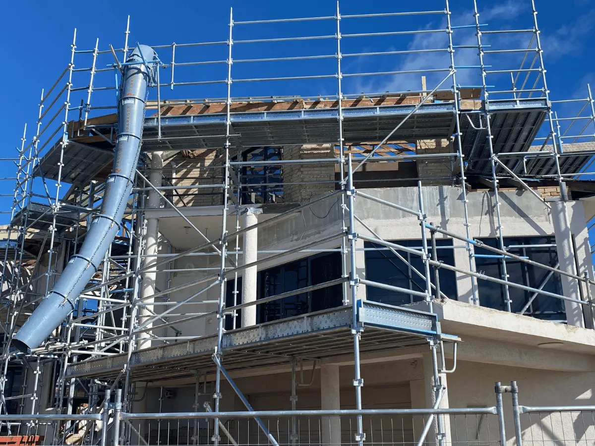 Enclosed waste bin chute attached to scaffold on a construction site