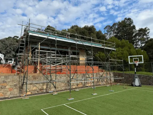 Roof-level scaffold around a stone-clad home with a backyard basketball court in Margaret River